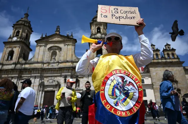 Homem com bandeira da Colômbia e um cartaz que diz "sim à consulta popular"