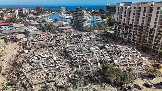 Sağda ayakta duran çok katlı bir bina, solda tamamen yıkılmış en az beş çok katlı apartman.