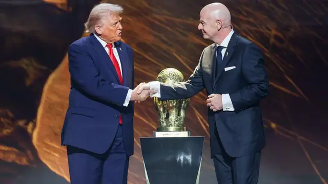 台の上に置かれたW杯のトロフィーの前で、スーツ姿のトランプ氏とインファティーノ氏が握手をしている