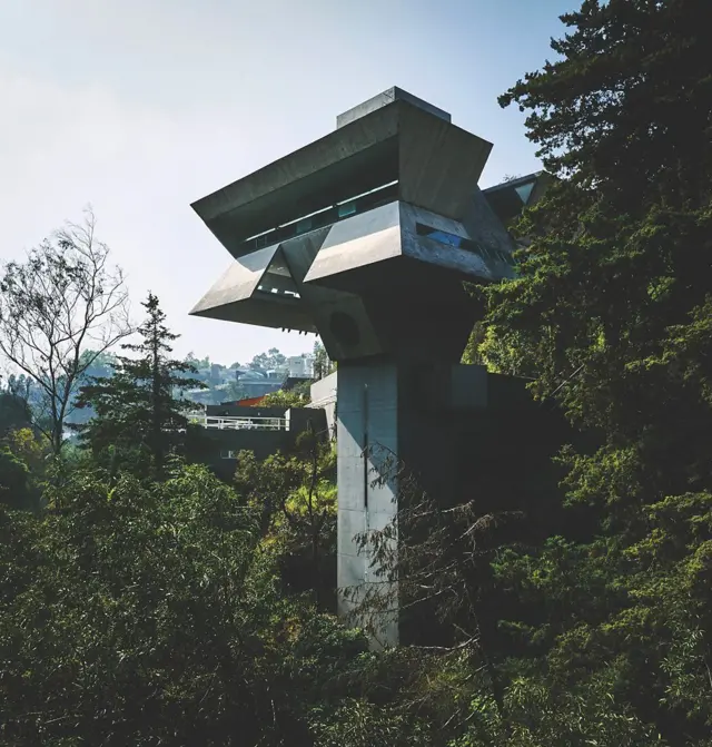 Estructura de hormigón brutalista elevada entre árboles sobre una ladera urbana.