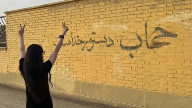 زن جوان بی حجاب در برابر دیوارنوشته تبلیغ حجاب