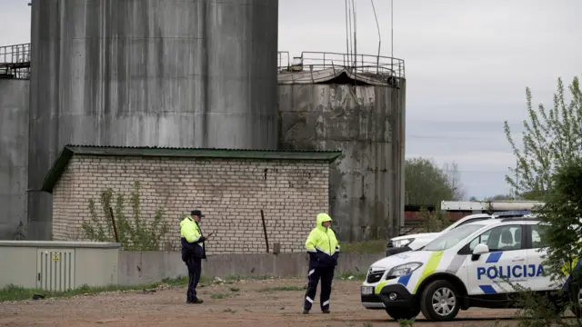 Двое полицейских и полицейская машина возле серых резервуаров