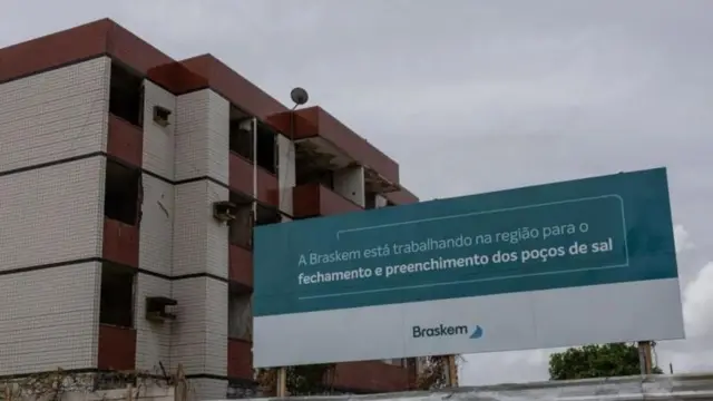Placa ao lado de prédio diz: A Braskem está trabalhando na região para o fechamento e preenchimento dos poços de sal