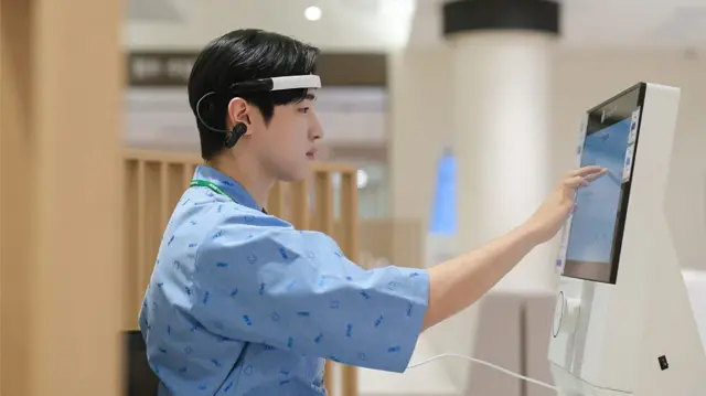 Jovem oriental com roupa de paciente de hospital toca com o dedo em uma tela