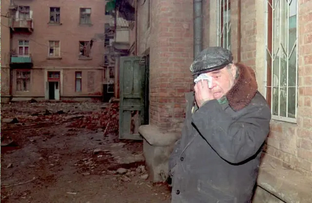 Пожилой мужчина плачет на фоне разрушенного дома