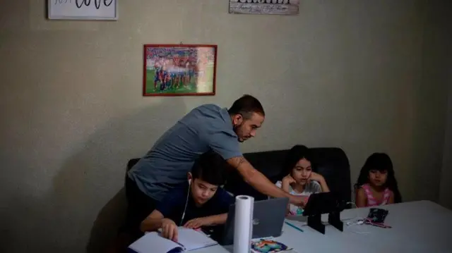 Seorang ayah berusia 34 tahun Carlos Aparicio membantu anak-anaknya Alessandro, Emmilia dan Emma selama kelas online.