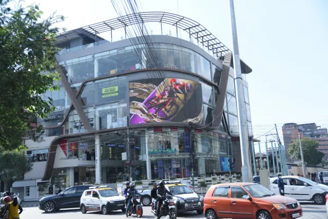  दरबार मल बाहिरको सडकमा ट्याङ्कसी र मोटरसाइकल गुडिरहेको दृश्य, एक जना प्रहरी ड्युटीमा खटिएको देखिन्छन्