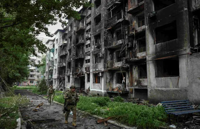 Двоє військових йдуть на фоні знищеного будинку