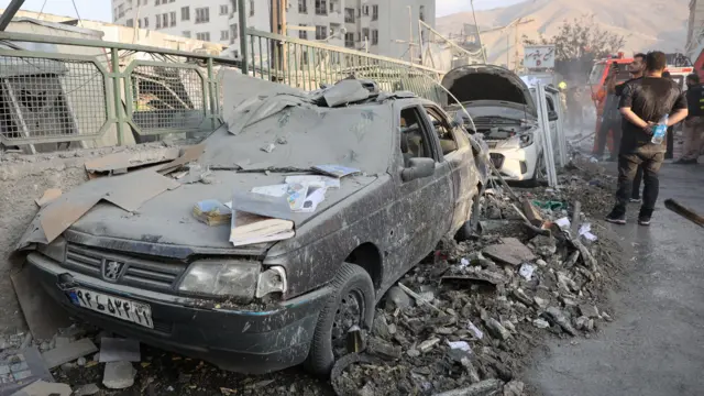 Wasu mutane sun taru a kusa da wata mota da hare-haren Isra'ila suka lalata a birnin Tehran.