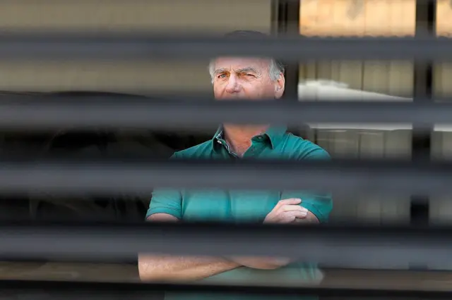 Bolsonaro, evinin bahçesinde, kepenklerin arasından çekilmiş bir fotoğraf.