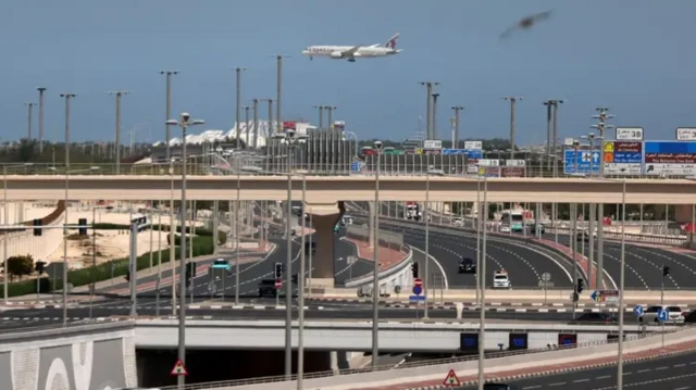 پل‌های سیمانی چند طبقه، خودروها در حال عبور و مرور هستند و یک هواپیما در حال پرواز در آسمان دیده می‌شود