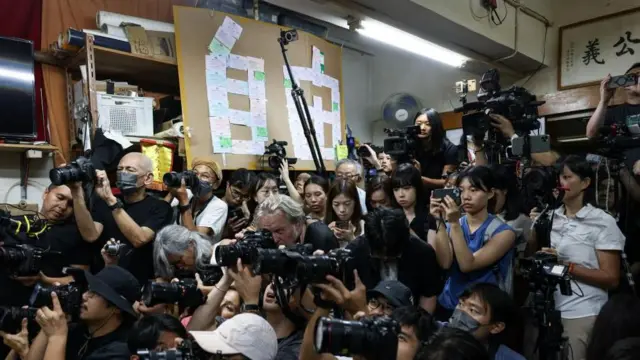 集まった報道陣が折り重なるようにカメラを構える後ろに、裁判傍聴券で「自由」の漢字を形作ったダンボールパネルが見える