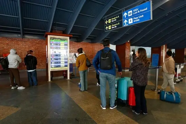 त्रिभुवन अन्तर्राष्ट्रिय विमानस्थलमा उडानहरूको विवरण हेर्दै विदेश जान लागेका मानिसहरू 