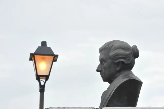 Busto de Cora Coralina com luminária antiga ao fundo