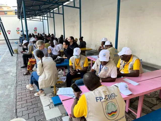 Les observateurs nationaux et internationaux attendent le démarrage du scrutin assis sur des bancs dans un centre de vote