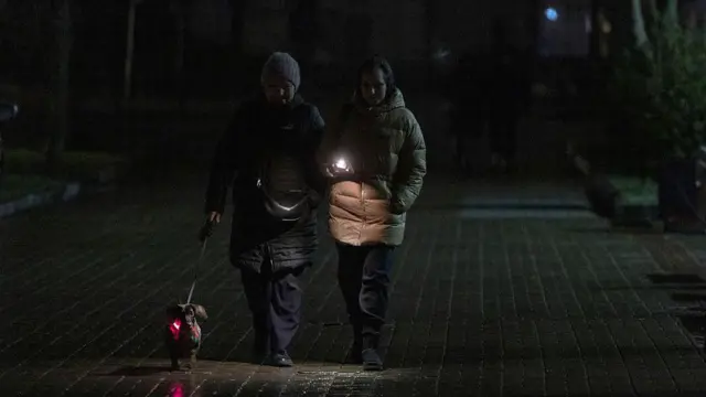 Дві жінки з собачкою і ліхтариком йдуть темною вулицею міста