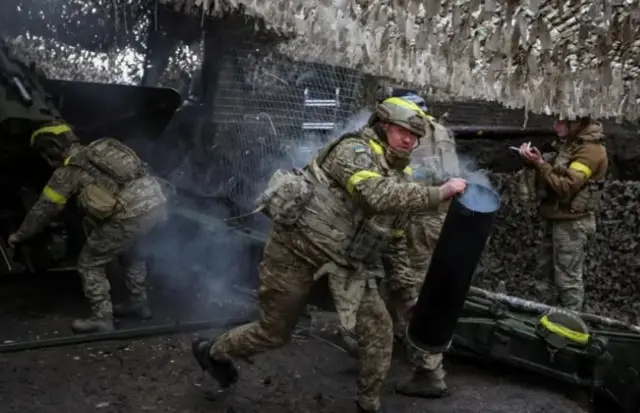 Українські військові у формі, бронежилеті, касці, ведуть запеклі бої під Куп'янськом. Військовий біжить у кадрі і дивиться у камеру прямо