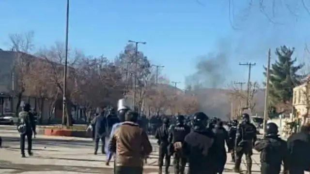 نیروهای امنیتی ایران در محل اعتراضات. در پس زمینه تصویر دود بلند است. 