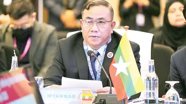ပြည်ထဲရေးဒုဝန်ကြီးဟောင်း ဗိုလ်ချုပ်အောင်ကျော်ကျော်ကို အနောက်တိုင်းဝတ်စုံနဲ့တွေ့ရပြီး ရှေ့မှာ အလံတိုင်ချထားပါတယ်။