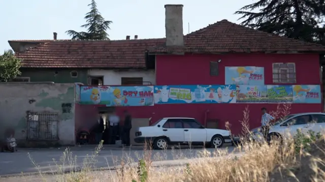 مبنى مكون من طابقين، جدرانه مطلية باللون الأحمر والأبيض والأخضر. هناك صور مرسومة على الجدران للبط والأطفال مع شعارات تروج للحليب وتطلب من الناس تناول المزيد من الفواكه والخضروات. الصورة التقطت في النهار والسماء زرقاء صافية.