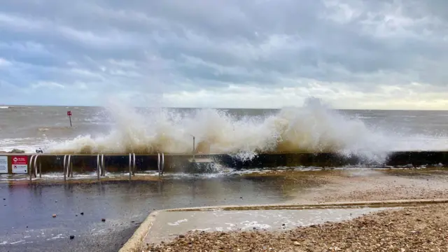 Las olas rompen contra un muro junto al mar. Hay charcos al otro lado.