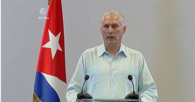 Gömlekli Küba Devlet Başkanı televizyonda konuşuyor yanında bayrak var.