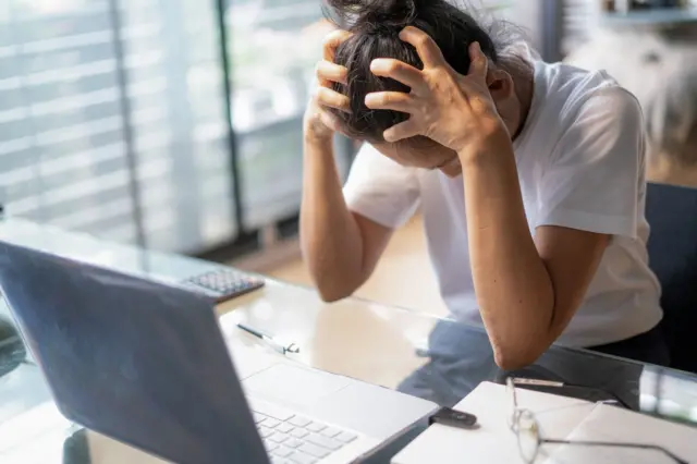 سيدة أعمال متعبة تعاني من صداع أثناء استخدامها لجهاز كمبيوتر محمول في مكتبها- صورة فوتوغرافية. 