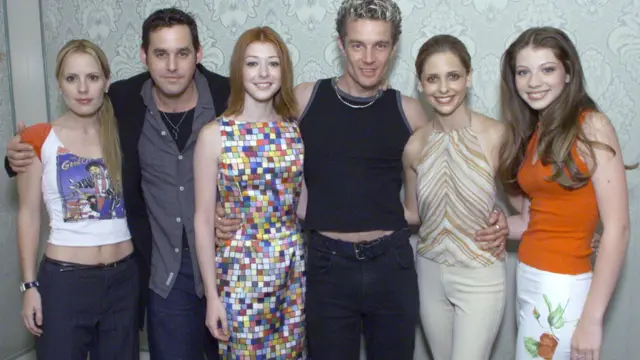 Les acteurs de Buffy (de gauche à droite) Emma Caulfield, Nicholas Brendon, Alyson Hannigan, James Marsters, Sarah Michelle Gellar et Michelle Trachtenberg photographiés ensemble en 2001. Trachtenberg porte un haut orange et un pantalon blanc à fleurs.