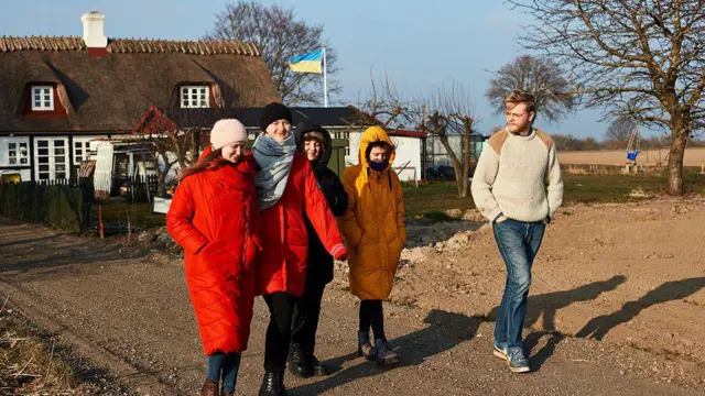 Четверо жінок та чоловік ідуть дорогою на тлі будинку з українським прапором