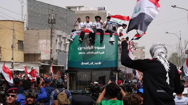 حافلة خضراء تقل لاعبي منتخب العراق، تحيط بها الجماهير وأعلام البلاد في شوارع بغداد، خلال الاحتفالات بالتأهل إلى كأس العالم 2026.