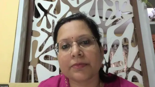Dr. Monika Anant terlihat sedang melakukan panggilan video di depan jendela.