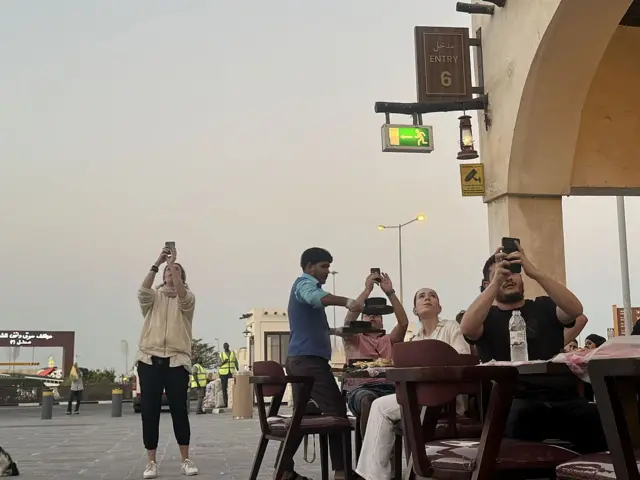 Люди за столиками кафе фотографируют работу ПВО в Дохе 28 февраля