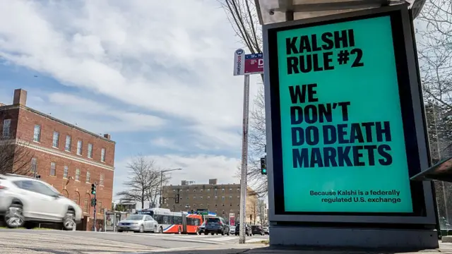 Anuncio en fondo verde con letras negras que dice, en inglés: "Kalshi Regla #2: No ofrecemos mercados de la muerte". Está en la pared lateral de una parada de autobús, se ve la calle, con algunos autos, dos edificios al frente y el cielo azul con nubes blancas