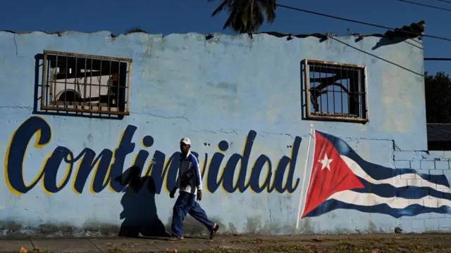 Um homem passa por uma parede pintada com a bandeira cubana que diz "Continuidade"casas de apostas valor minimo 1 realHavana