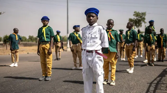 Young boys in scouts' uniforms stand on the road in a neat formation
