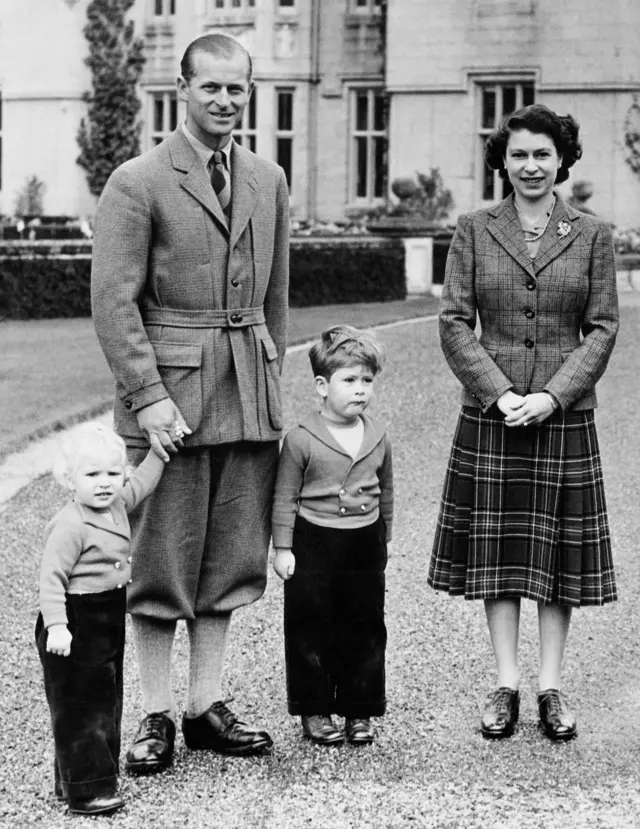 Молодая королева в другом твидовом блейзере в клетку и более темной юбке в шотландскую клетку до колен в компании герцога Эдинбургского, принца Чарльза и принцессы Анны в замке Балморал в сентябре 1952 года