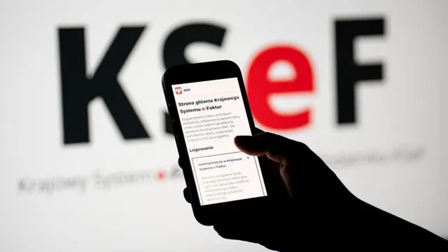 Strona internetowa Krajowego Systemu e-Faktur jest wyświetlana na ekranie telefonu komórkowego, a logo KSeF jest widoczne na ekranie komputera w Krakowie
