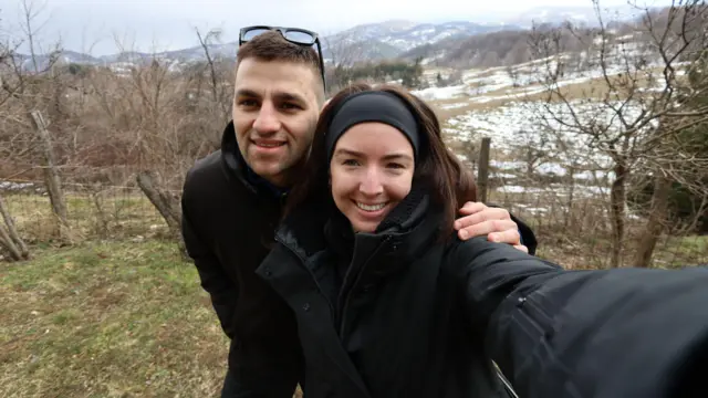 Sophia ve Pedja bir selfie fotoğrafında kameraya gülümsüyorlar. Dışarıdalar, üzerinde biraz kar olan çimenli bir tepede. Her ikisi de siyah ceketlerle sarılmış. Pedja"nın kısa kahverengi saçları var, ve Sophia"nın uzun kahverengi saçları var, ve siyah bir kafa bandı takıyor. 