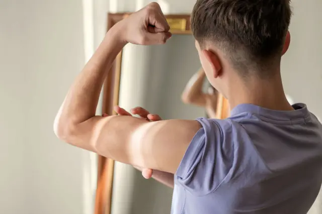 Adolescente se olhando no espelho e tentando forçar os músculos dos braços