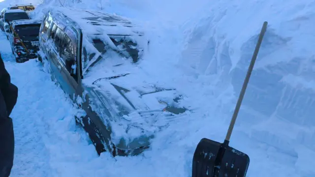 Джип в снегу, наполовину застрял в затердевшем сугробе. Перед джипом в сугроб воткнута лопата