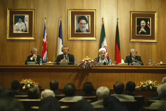 تهران، ایران: حسن روحانی، دبیر وقت شورای عالی امنیت ملی جمهوری اسلامی ایران، در ۲۱ اکتبر ۲۰۰۳ در کاخ سعدآباد تهران در حالی با خبرنگاران سخن می‌گوید که جک استراو وزیر خارجه بریتانیا (چپ)، دومینیک دو ویلپن وزیر خارجه فرانسه (نفر دوم از چپ) و یوشکا فیشر وزیر خارجه آلمان (راست) به سخنان او گوش می‌دهند. ایران در بیانیه‌ای مشترک پس از مذاکرات با وزیران خارجه بریتانیا، فرانسه و آلمان، متعهد شد که شفافیت کامل در تعامل با نهاد نظارتی هسته‌ای سازمان ملل (آژانس بین‌المللی انرژی اتمی) داشته باشد و تأکید کرد که سلاح هسته‌ای «هیچ جایگاهی» در دکترین دفاعی این کشور ندارد. (عکس از عطا کناره / خبرگزاری فرانسه از طریق گتی ایمجز)