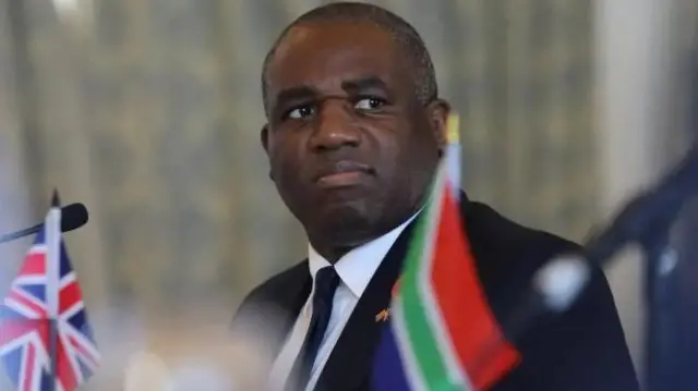 David Lammy yambaye  ikoti yirabura n'ikaruvati, ariko araraba  muri kamera