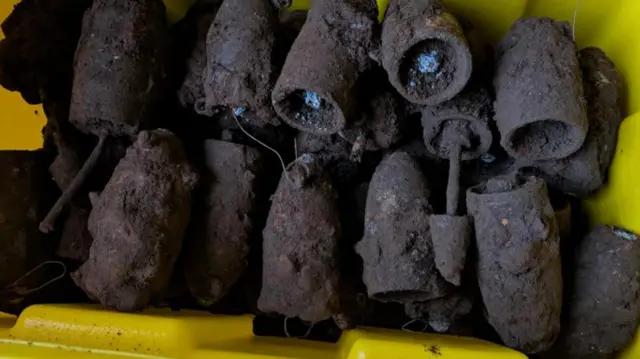 Uma caixa amarela com cerca de 20 bombas da Segunda Guerra Mundial cobertas de lama, mas com uma carga ainda visível na maioria delas