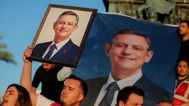 Elinde ÖZgür ÖZel fotoğrafı olan bir erkek görüyoruz. Yanında bir kadın var.
