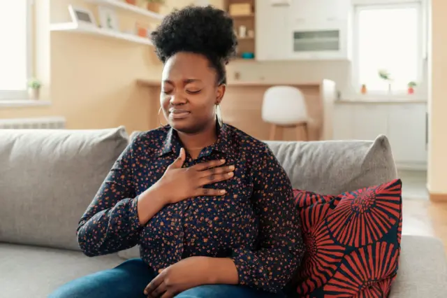 Photo en gros plan d'une femme afro-américaine obèse et stressée qui souffre d'une douleur thoracique et qui touche la région de son cœur.