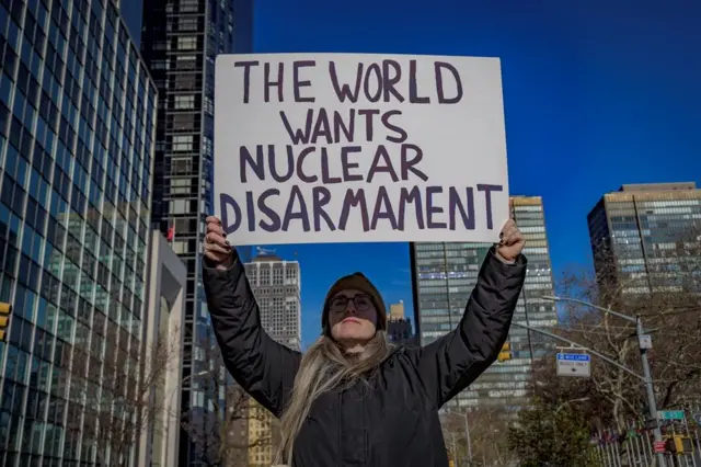 Um manifestante de jaqueta preta segura uma faixa que diz: "O mundo quer desarmamento nuclear".