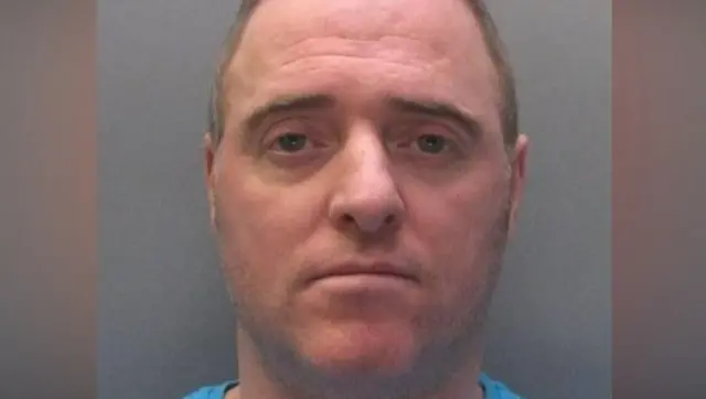 McDonald patrzy ponuro w obiektyw. Ma brązowo‑siwe włosy i kilkudniowy zarost.