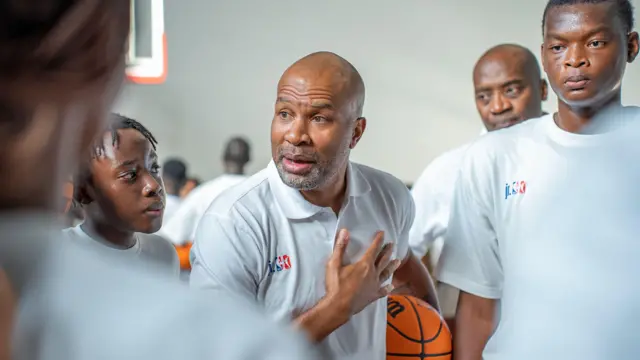 Derek Fisher (au centre) tient un ballon de basket sous son bras pendant une conférence aux jeunes lors d’une séance d’entraînement au Kenya