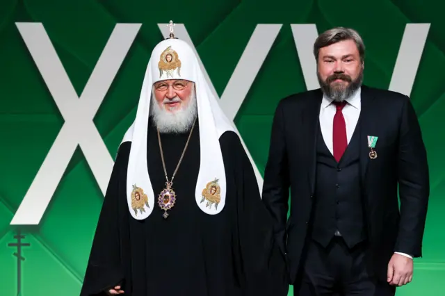 Патриарх Кирилл и Константин Малофеев стоят на зеленом фоне с надписью XXV