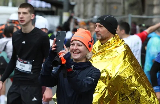 žena fotografiše dok je iza nje muškarac sa pokrivačem